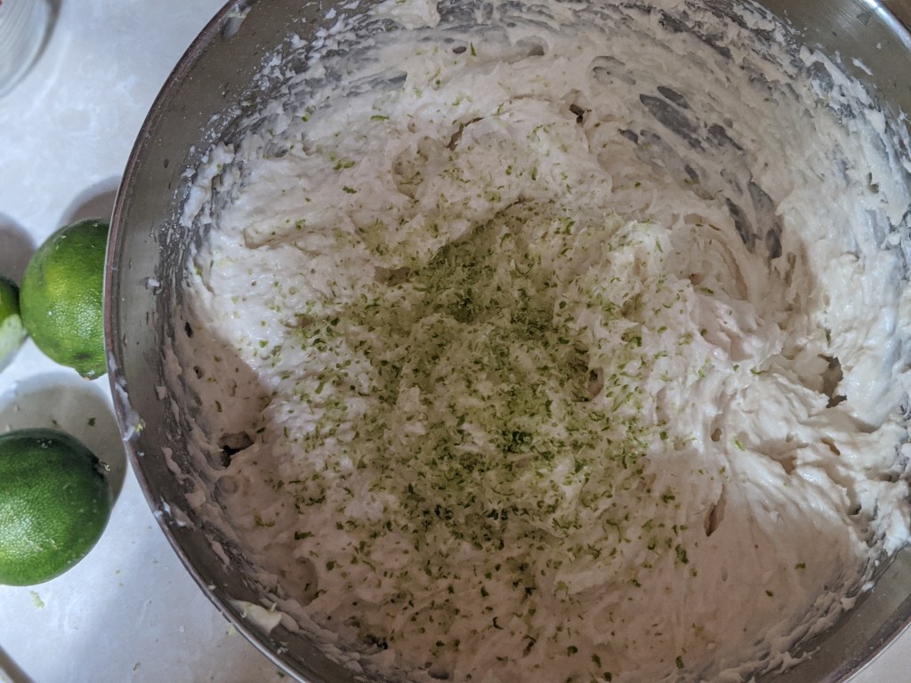 Cake batter mixed with dry ingredients and lime zest. Photo shows creamy white batter with bright green specks of lime zest.