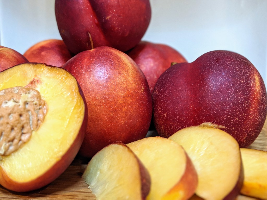 Pile of ripe nectarines, one sliced open showing the soft, yellow center. Slices of nectarine to the side