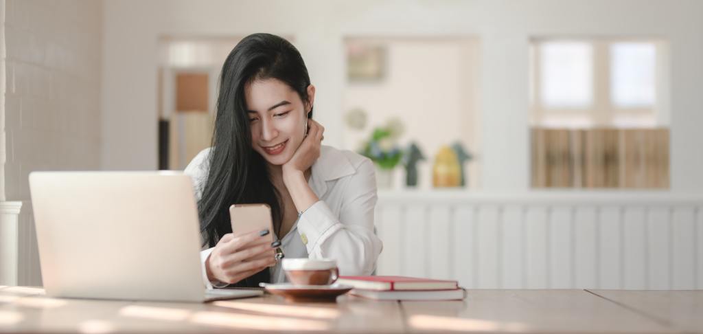 image of a woman using a phone and computer. Woman represents a seller looking for a real estate agent in the Albuquerque area