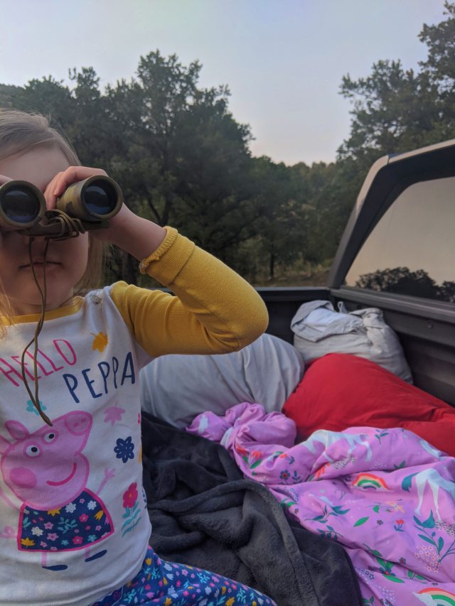 My three year old sitting in a truck bed and looking through binoculars