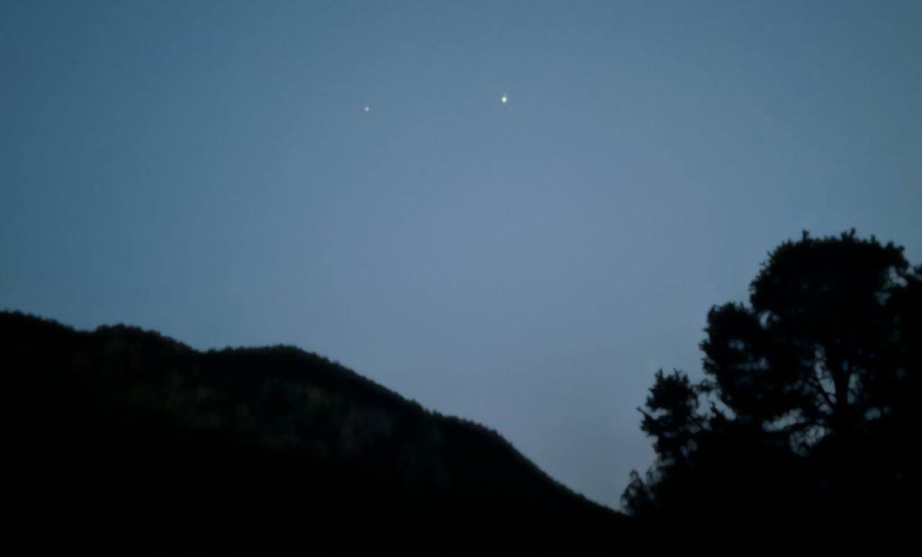 Twilight photo of Jupiter and Saturn emerging. Trees and mountains in the shadows
