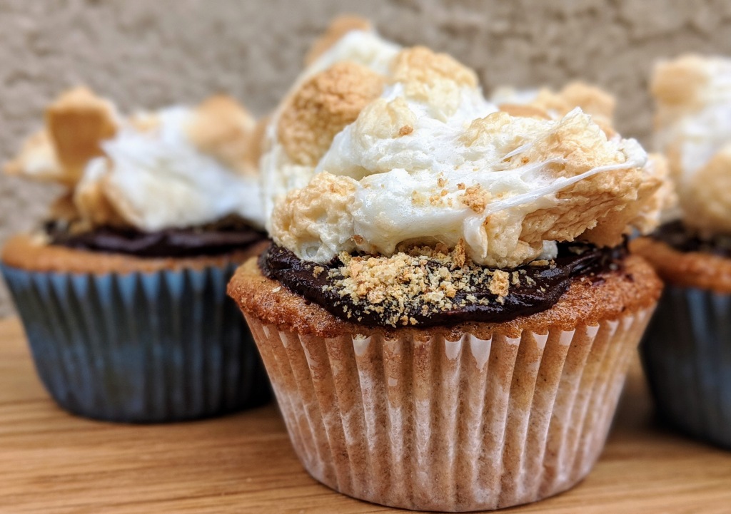 Final S'more cupcake against an adobe wall. Cupcake filled with chocolate, topped with chocolate, graham cracker, and marshmallow