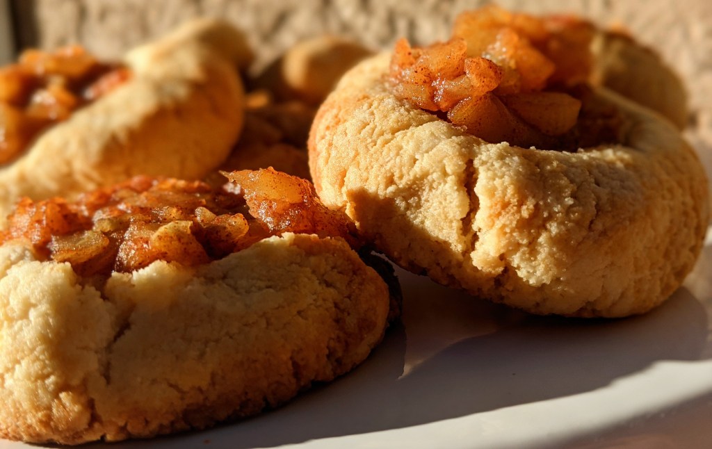 Cookies filled with apple pie filling jam basking in the sunlight. The light makes both the cookie and filling have a golden glow