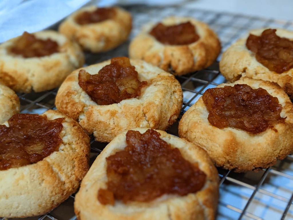 Cookies fresh from the oven. Golden edges and oozing with jam filling. Cookies in a line on top of a cooling rack.