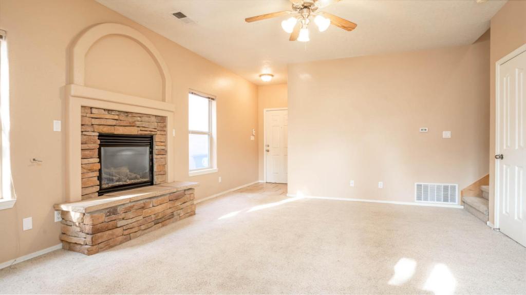 Interior shot of the living and family room with a stone fireplace focal point. Beighe carpet and tan walls.